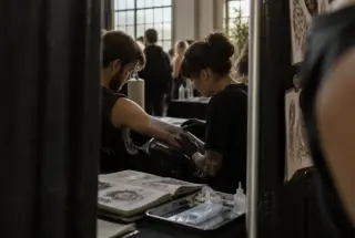 Visitor’s-eye view of a tattoo artist and client discussing stencil placement at a convention workspace.